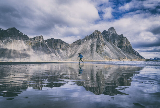 冒险穿着蓝色衬衫和黑色裤子的人站在山下湖边的蓝色皮艇上自然冰川户外