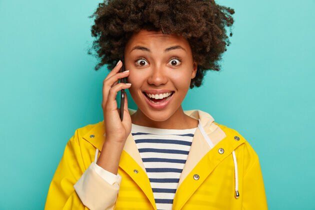 女人一个皮肤黝黑 穿着条纹套头衫和黄色雨衣的年轻女子用手机拍摄了一张不规则的照片微笑交谈呼叫