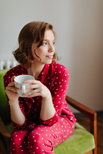 休闲穿着红色睡衣的梦幻少女手里拿着一杯咖啡室内拍摄的是坐在扶手椅上沉思的女人 目光移开了睡衣寒冷饮料