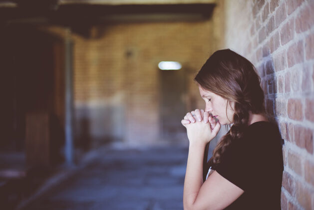 人类靠着砖墙祈祷的女人模特美丽信仰