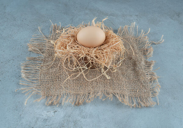 有机在大理石背景上的一小堆稻草上放一个鸡蛋高质量的照片美味早餐配料