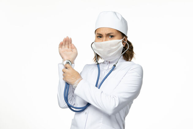 听诊器正面图年轻女医生戴防护面罩因冠状病毒在白色表面使用听诊器防护病毒冠状病毒