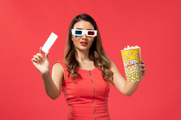 电影院正面图：红色表面上戴着d墨镜拿着爆米花的年轻女性前面票爆米花