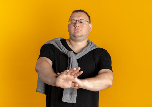 制造一个戴眼镜 身穿黑色t恤 表情严肃的超重男子站在橙色的墙上做停车标志脸站男人