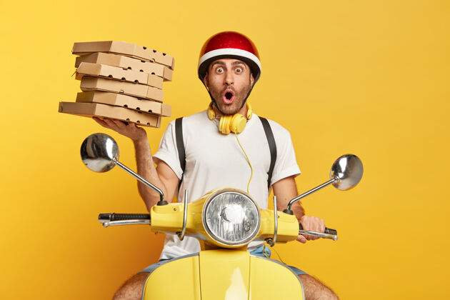 送货带着头盔的送货员手持披萨盒 驾驶着黄色滑板车 震惊不已食物车辆耳机