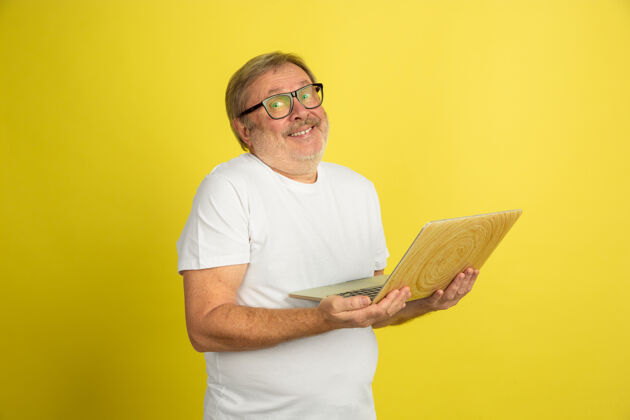 白色使用笔记本电脑 微笑白人男子肖像隔离在黄色工作室背景美丽的男模特在白色衬衫摆姿势时尚男士情绪