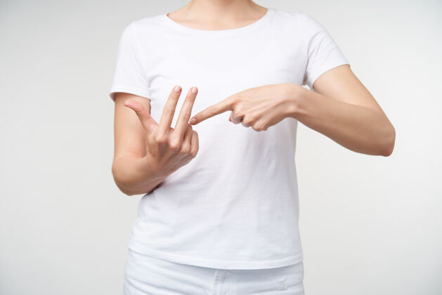 白色室内拍摄的年轻女性穿着休闲服举手 同时用手语交谈 显示在白色背景上摆姿势时数单词身体文字女士