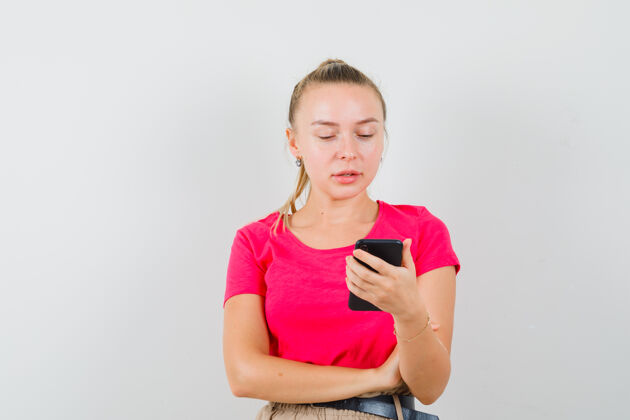 成人年轻的女士看着手机 穿着粉红色的t恤 神情沉思快乐外观手机