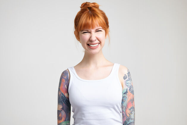 纹身年轻可爱的红头发女人纹身的摄影棚照片眯着眼睛 快乐地微笑着 在白色背景上摆姿势时精神抖擞鼻子微笑长