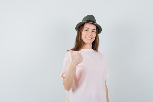 快乐穿着粉色t恤的年轻女孩 戴着一顶大拇指朝上的帽子 看上去很快乐 正面视图可爱年轻积极