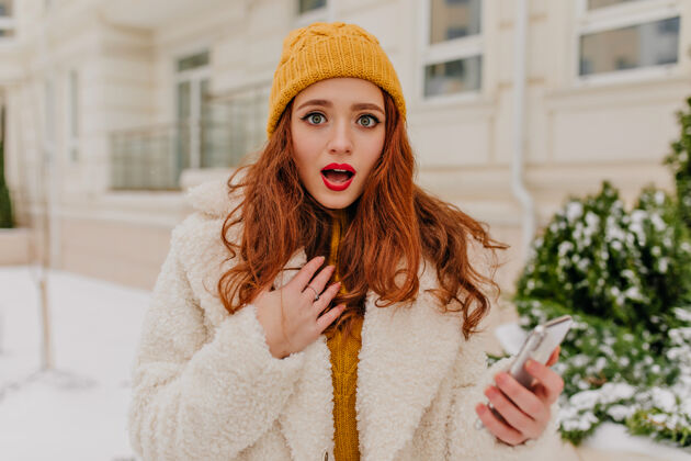 雪冷天里站在街上的姜姑娘大吃一惊漂亮的年轻女子拿着手机在户外摆姿势女性深色冬季