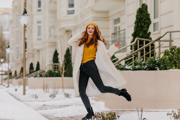 户外无忧无虑的女孩在冬日里滑稽地跳舞穿着白大褂的迷人的姜女的户外照片表达雪散步