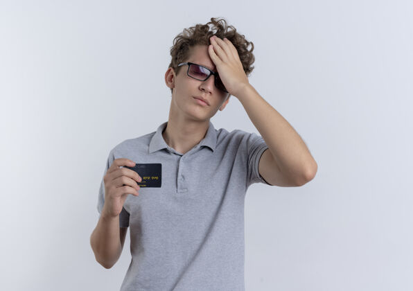男人一个戴着黑眼镜 穿着灰色马球衫的年轻人站在白墙上 脸上露出信用卡的困惑和焦急困惑焦虑显示