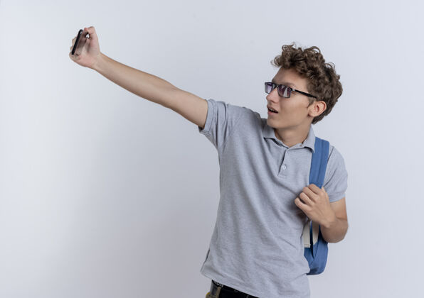 男人穿着灰色马球衫的年轻人拿着智能手机站在白墙上微笑着自拍站着自拍马球