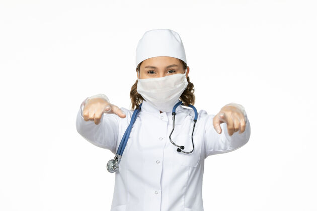 大流行正面图年轻女医生由于白色表面有冠状病毒 戴着无菌口罩和手套听诊器疾病制服