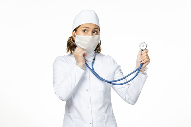 医院正面图年轻女医生戴无菌口罩因冠状病毒在白色表面使用听诊器大流行听诊器疾病