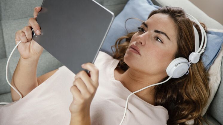平板电脑戴耳机的女人用平板电脑在线流流室内