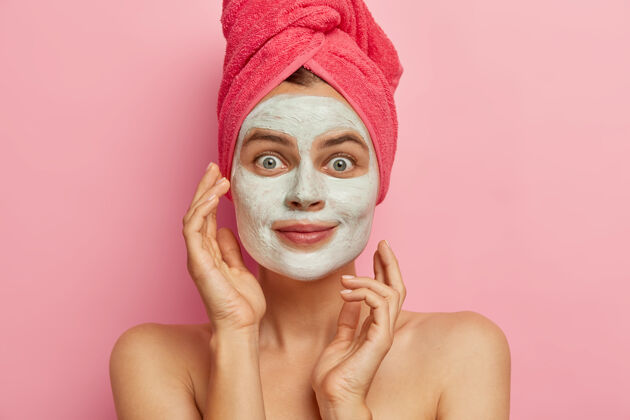 治疗可爱的年轻女子照片为脸部护理应用营养面膜 要有干净新鲜的皮肤 头上戴粉色毛巾裸体看柔软