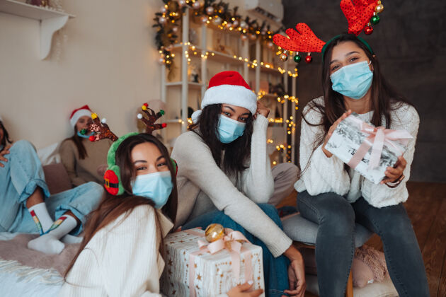 流行病戴着圣诞帽的多民族朋友们微笑着 手里拿着礼物对着镜头摆姿势在冠状病毒的限制下庆祝新年和圣诞节的概念检疫中的节日帽子朋友隔离