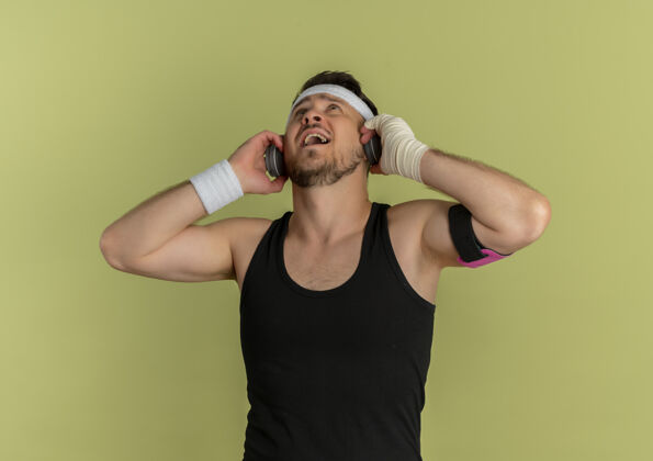 橄榄戴着头带和耳机站在橄榄色背景下听音乐的年轻健身男子站耳机听