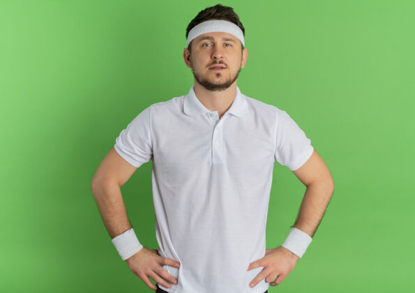 表情身穿白衬衫 头戴头巾的年轻健身男子站在绿色背景下 自信地看着镜头自信头带白色