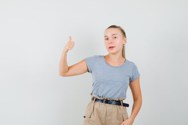 时尚年轻的女性在t恤衫 裤子上竖起大拇指 看起来很快乐 正面视图人肖像黑发