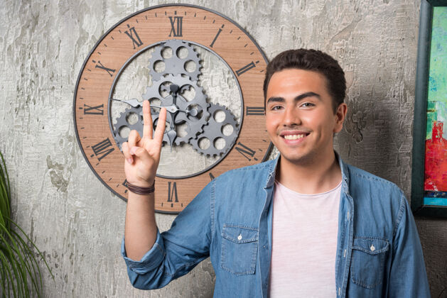 男人年轻人伸出两个手指在大理石背景上摆姿势高质量的照片时钟男人摆姿势