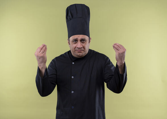 烹饪心烦意乱的男厨师身穿黑色制服 头戴厨师帽 看着镜头困惑的手势 双手站在绿色背景上男性绿色手势
