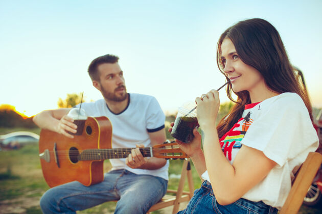 啤酒在河边的夏日里 一对情侣坐在沙滩上休息 弹吉他爱情 幸福的家庭 度假 旅游 夏日概念白种人男女夜晚一起自然