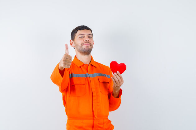 办公室年轻的工人手持红心 穿着制服竖起大拇指 看上去很高兴沟通工业团队合作