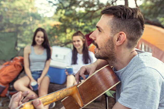 夫妇聚会 男女露营在森林里他们放松 唱着歌对抗绿草度假 夏天 冒险 生活方式 野餐的概念食物旅行放松