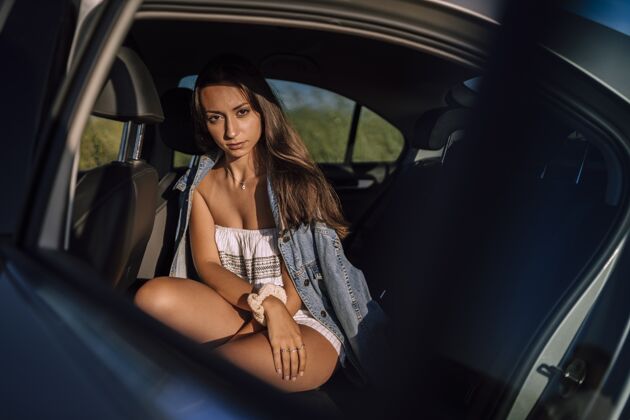 模型一个美丽的年轻白人女性在一个领域的汽车后座摆姿势的水平镜头车辆阳光站立