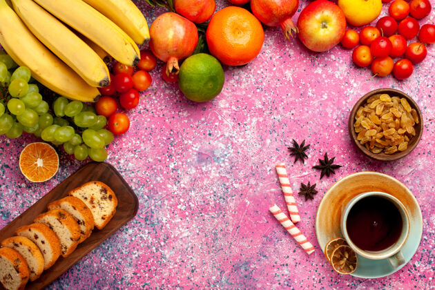 蛋糕俯瞰美味的水果组成与切片蛋糕和一杯茶在粉红色的桌子上新鲜维生素食物
