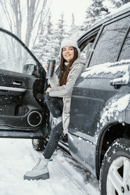 汽车侧视图笑脸女子享受雪 而在公路旅行 并有一个温暖的饮料冬天户外公路旅行