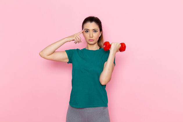健身正面图年轻女性手持哑铃在浅粉色墙上运动员运动锻炼健康锻炼抱人前面