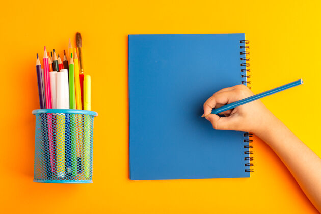 办公室俯视图：小孩在橘色表面的文案上画画和写东西写作钢笔绘画