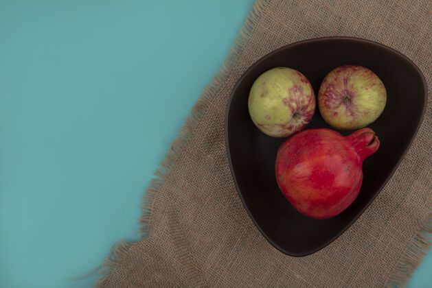 蓝色新鲜石榴与苹果在一个碗上的一个袋子布上蓝色背景与复制空间的顶视图空间新鲜碗