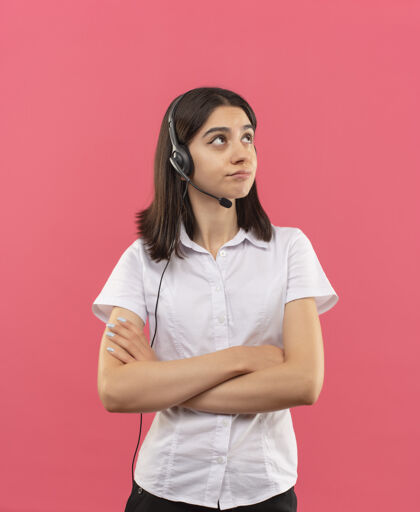 表情一个穿着白衬衫戴着耳机的年轻女孩站在粉红色的墙上 神情沉思地看着一边沉思女孩站着