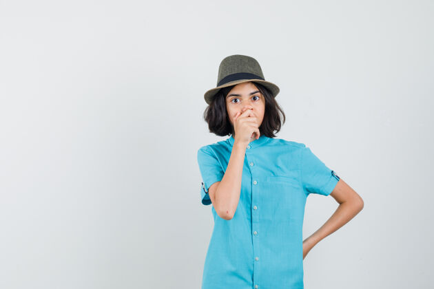 女性穿着蓝色衬衫 戴着帽子 手放在嘴上的年轻女士看起来很担心女人乐趣嘴