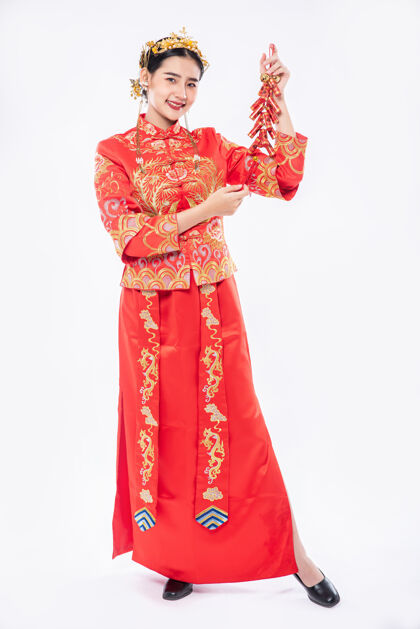 旗袍女人穿旗袍套装微笑着从亲戚那里得到鞭炮在中国新年中国新年中国民族女孩