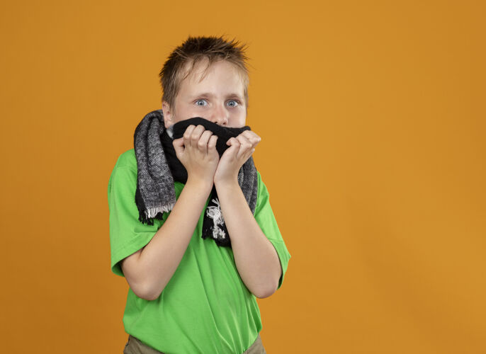 围巾生病的小男孩穿着绿色t恤 脖子和嘴上围着温暖的围巾 惊恐地站在橙色的墙上疾病温暖橙色