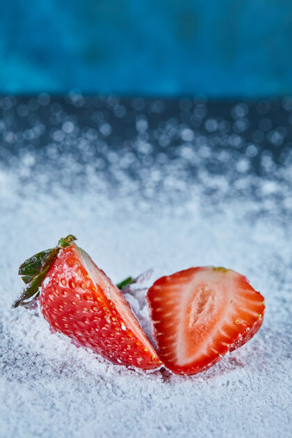 成熟新鲜草莓片在蓝色的表面与粉末草莓叶美味