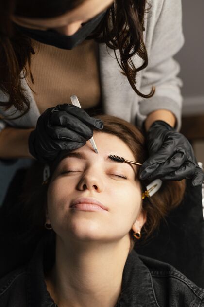面膜高角度的女临床医生为女性做美眉治疗眉毛美容师头发