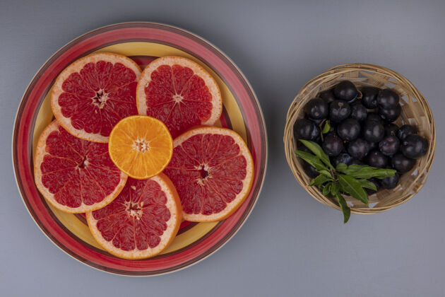 切片俯视图柚子片放在盘子里 樱桃李子放在篮子里 背景是灰色的水果盘子葡萄柚