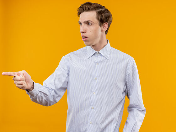 指着穿着白衬衫的年轻人用指南针指着站在橙色墙上的困惑的东西站着男人橙色