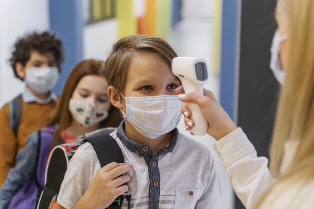 冠状病毒带着医用面罩的女老师在学校检查学生的体温学习返校知识