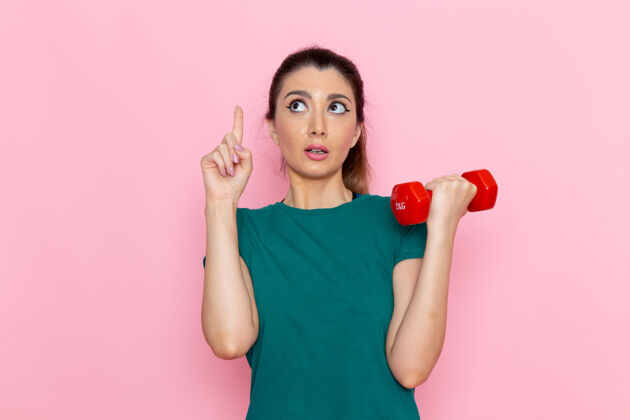 观点正面图年轻女性手持哑铃在粉红色的墙上运动员运动锻炼健康锻炼人可爱前面