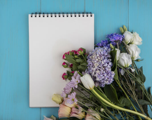 顶部蓝色背景上的花卉和便笺簿顶视图 带复印空间笔记便笺空间