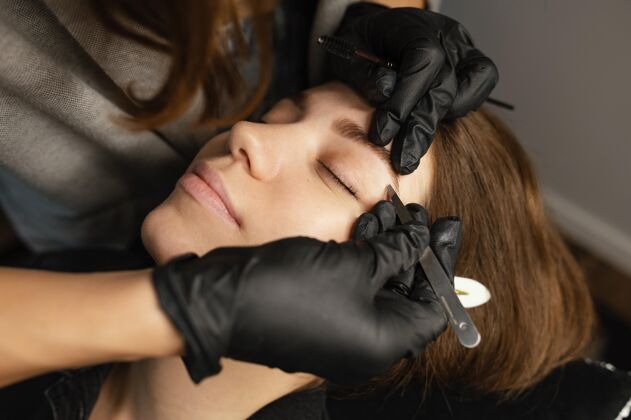 乳胶手套高角度的女美容师为女性做美眉治疗专家镊子女人
