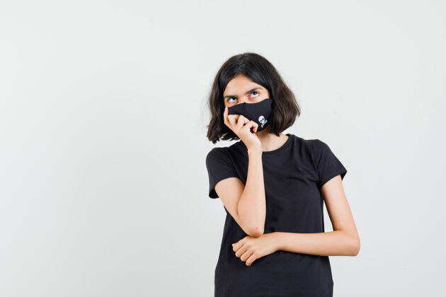 时尚穿着黑色t恤的小女孩 戴着面具站在思考的姿势 正面视图未成年站立青年